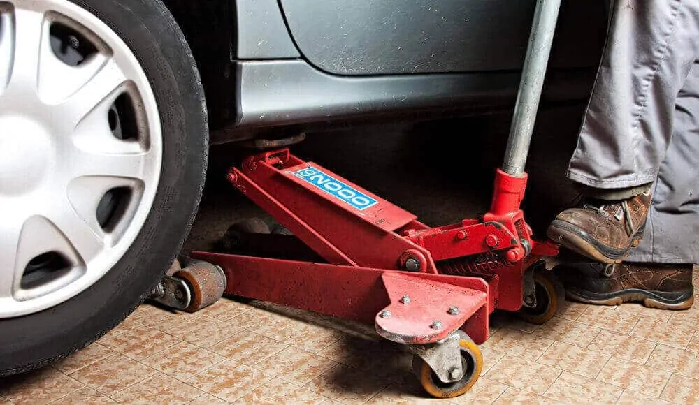 Mechanic is lifting the hydraulic floor jack under a car.