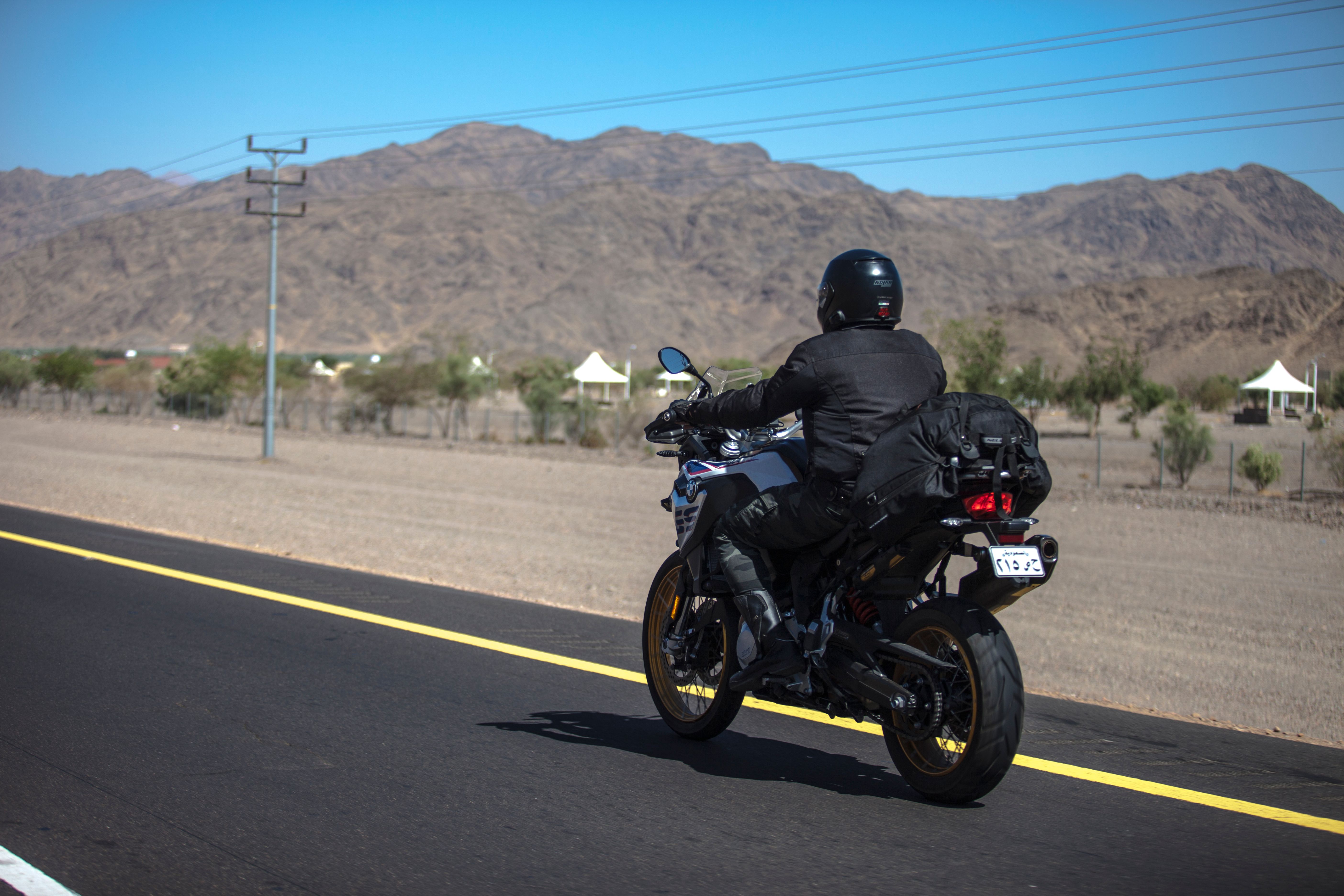 Motorcyclist riding along a scenic desert highway framed by arid mountains on a long-distance journey