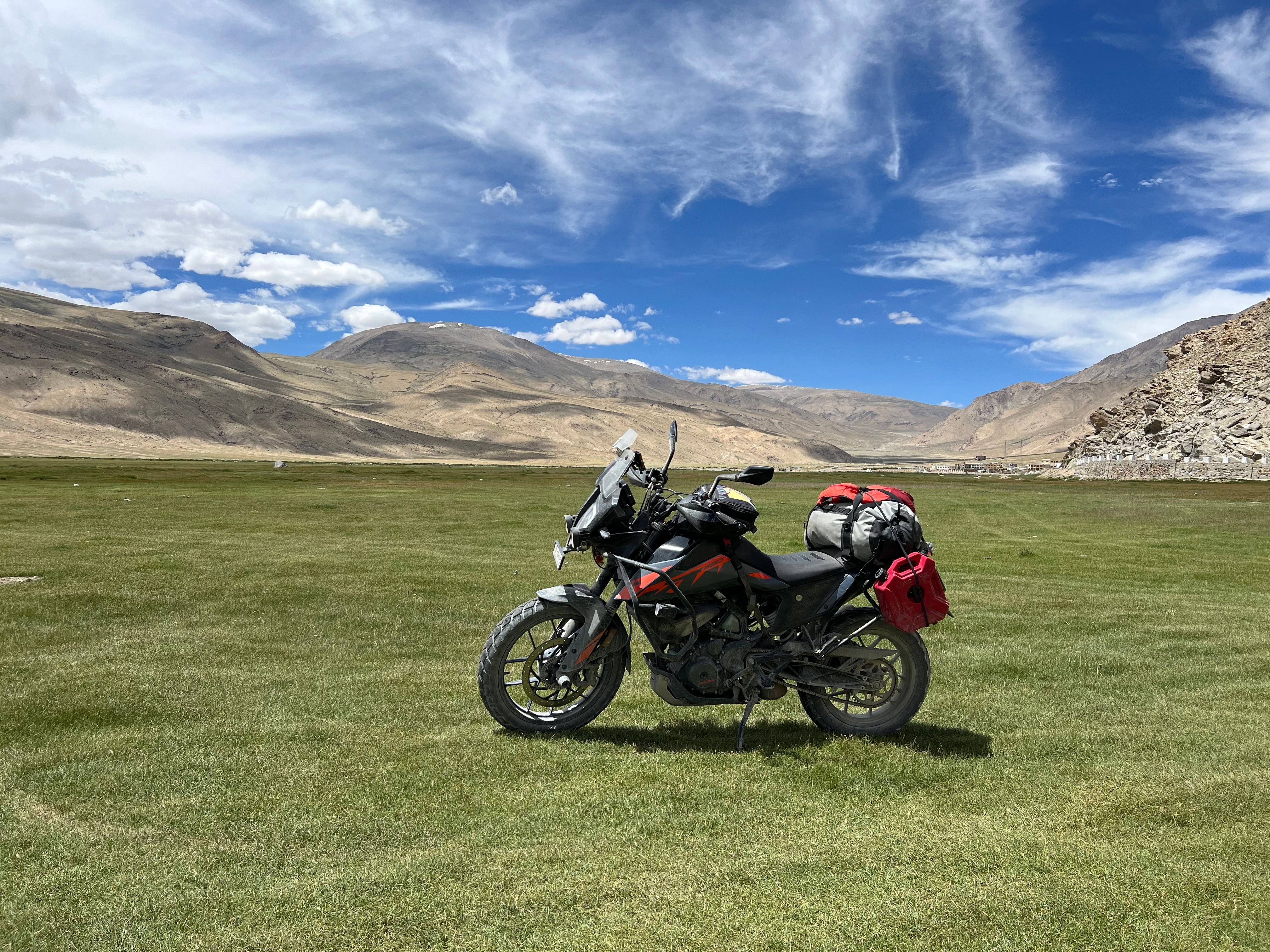 Motorcycle loaded with travel luggage and gear standing in a vast green landscape with mountains
